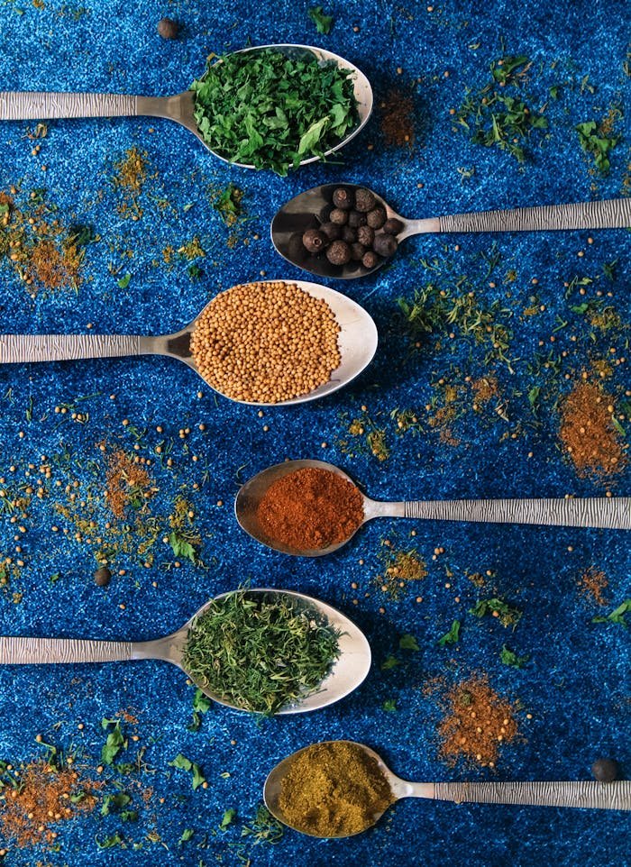 Colorful spices in spoons on a vibrant blue background, showcasing culinary variety.